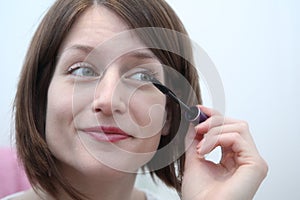 Young woman applying mascara in front of a mirror