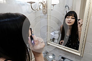 Young woman applying mascara in front of a mirror. Girl getting ready with her makeup in a hotel bathroom. Pretty female serious