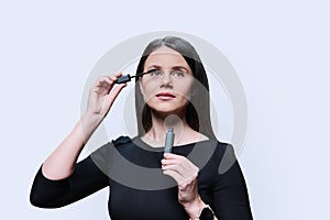 Young woman applying mascara on her eyelashes, on white background