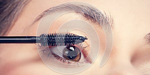 Young woman applying mascara to her lashes.