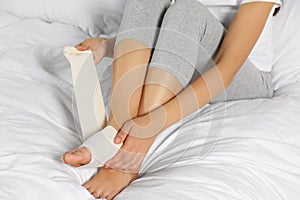 Young woman applying medical bandage onto foot on bed, closeup