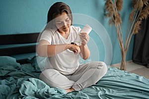 Young woman applying moisturizing hand lotion while sitting in her bed, body care