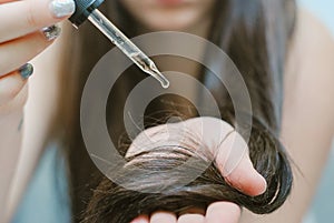 Young woman applying oil onto her hair, indoors photo