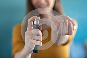 Young woman applying perfume on her wrist while standing at home