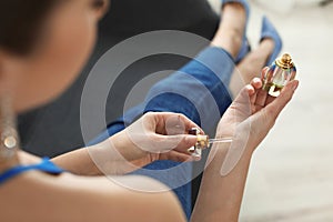 Young woman applying perfume on wrist against blurred background