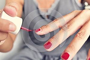 Young woman applying red nail polish to her fingernails