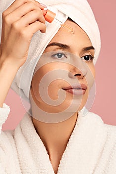 Young woman applying serum oil on face during skin care routine