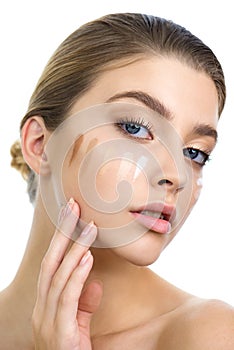 Young woman applying several color samples of facial foundation cream at her face
