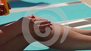 Young woman is applying sun cream on her legs by the pool on hot summer day.