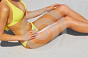 Young woman applying sunscreen on her leg on the beach
