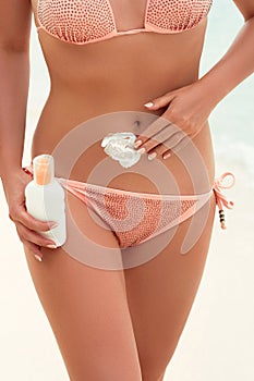 Young woman applying sunscreen lotion, holding sun cream bottle on the beach. Sun protection.