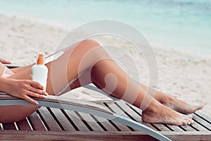 Young woman applying sunscreen lotion, holding sun cream bottle on the beach. Sun protection. Skin care