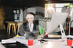 Young woman architect in black hat and leasure jacket working at the table. Photo of blond woman working with new