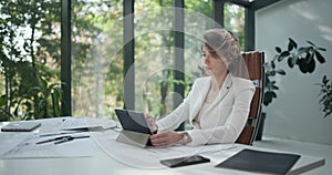 A young woman architect holding and working with tablet pc pad at her work office with big sunlight windows