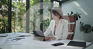 A young woman architect holding and working with tablet pc pad at her work office with big sunlight windows