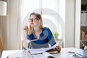 Young woman architect sitting at the desk indoors in home office, working.