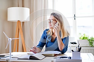 Young woman architect sitting at the desk indoors in home office, working.