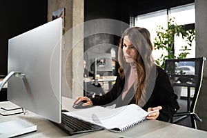 Young woman architect working with blueprints and technical design project at work table and computer in office