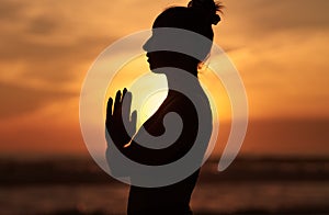 Young woman with arms in namaste against sunset sky