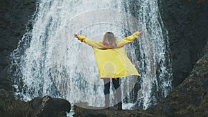 Young woman arms outstretched behind spectacular waterfall in Iceland. Shot of young woman outstretching arms by