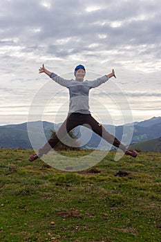 Young woman with arms outstretched jumping on the top of mountain. Success and winning concept. Active sport background.