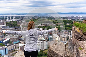 Young woman with arms raised on a hill over the city of Edinburgh