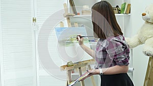 Young woman artist in apron painting picture on canvas in art studio