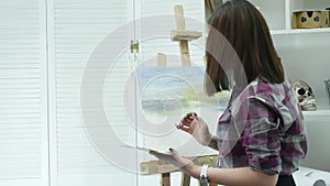 Young woman artist in apron painting picture on canvas in art studio