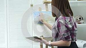 Young woman artist in apron painting picture on canvas in art studio