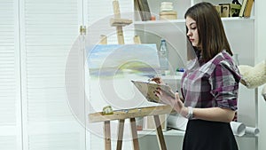 Young woman artist in apron painting picture on canvas in art studio