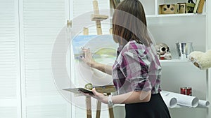 Young woman artist in apron painting picture on canvas in art studio