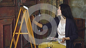 Young woman artist draw pictrure with watercolor paints and brush on easel canvas