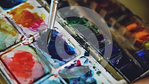 Young woman artist draw pictrure with watercolor paints. Closeup brush mixing colors in pallete