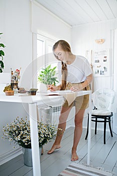 Young woman artist drawing on sheet, behind the table at home.