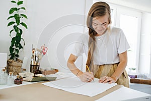 Young woman artist drawing on sheet, behind the table at home.