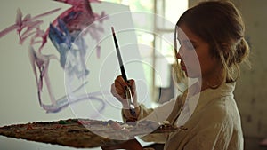 Young woman artist drawing in studio. Skilled painter using palette indoors.