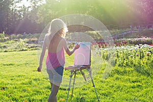 A young woman artist holds a brush and paints a picture on an ea
