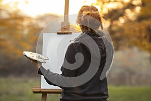 Young woman artist in nature drawing a picture on canvas on an easel in nature