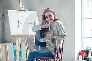 Young woman artist painting at home creative biting paint brush