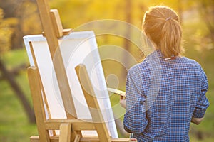 Young woman artist standing near an easel and looking at the sunset on the lawn, the girl is looking for inspiration for painting