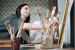 Young woman artist teenager girl student with dark long hair in casual draws picture at the art studio