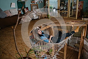 Young woman artist wearing overall resting in hammock at her studio