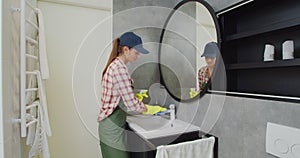 Young woman as a professional cleaner in uniform cleaning bathroom. Cleaning service concept.