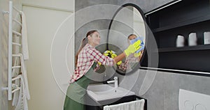 Young woman as a professional cleaner in uniform cleaning bathroom. Cleaning service concept.