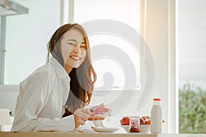 Young woman asia wake up refreshed in the morning and relaxing eat coffee, cornflakes, bread and apple for breakfast at house on h photo