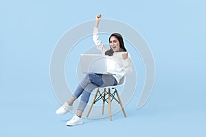 Young woman asian happy smiling celebrate. While her using laptop sitting on white chair isolate on bright blue background