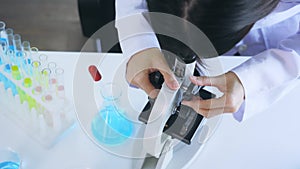 Young woman Asian scientist wearing medical labcoat performing research in lab while seeing elements through microscope