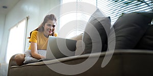 Young woman Asian using laptop pc computer on couch relax surfing the internet at home. lifestyle relaxation concept
