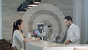 Young woman asking male barista for a bill and paying while sitting at cafe counter