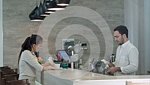 Young woman asking male barista for a bill and paying while sitting at cafe counter